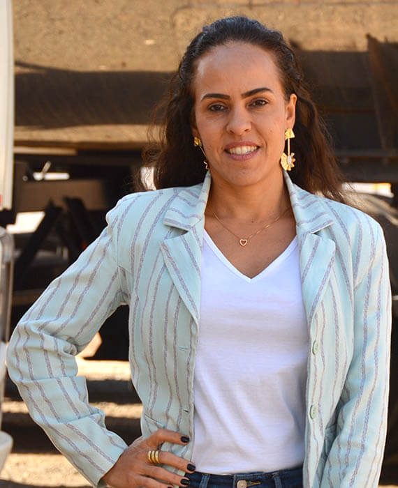 Mulher com blazer social e mão na cintura posando em frente ao caminhão que transporta gás industrial